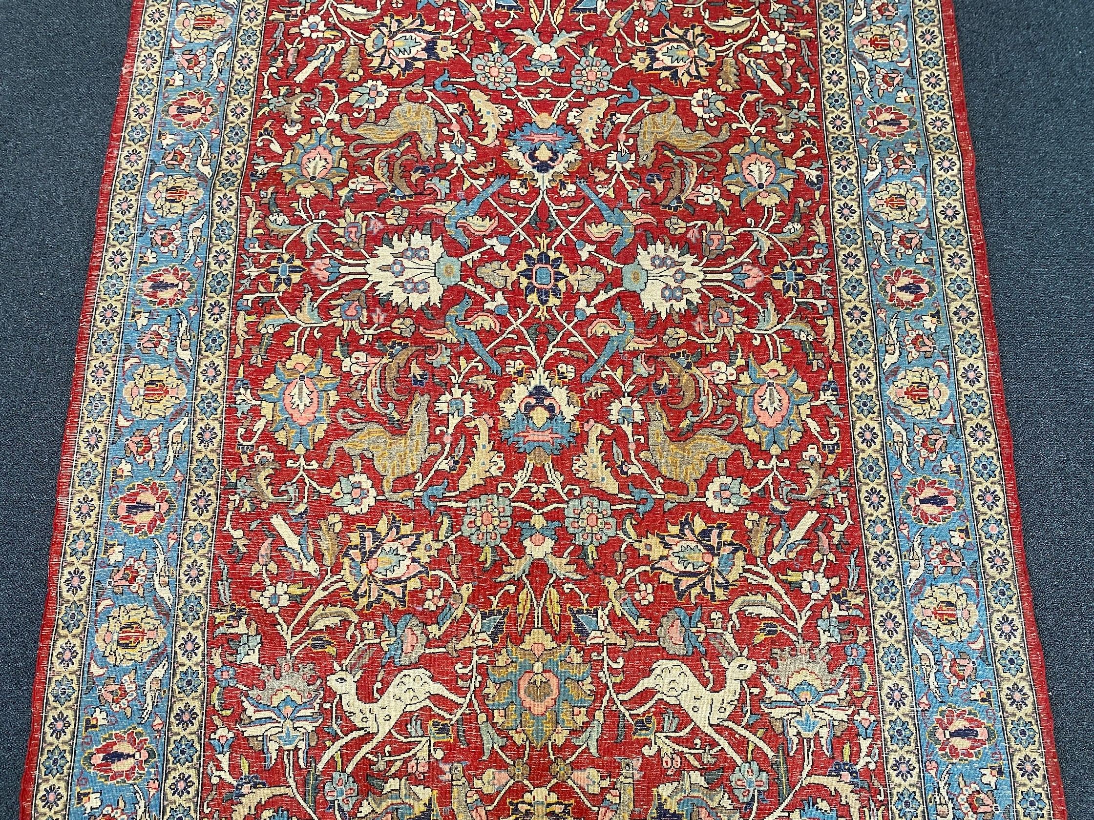 A Persian Qum red ground rug woven with animals and exotic birds among stylised flower heads 220 x 125 cms